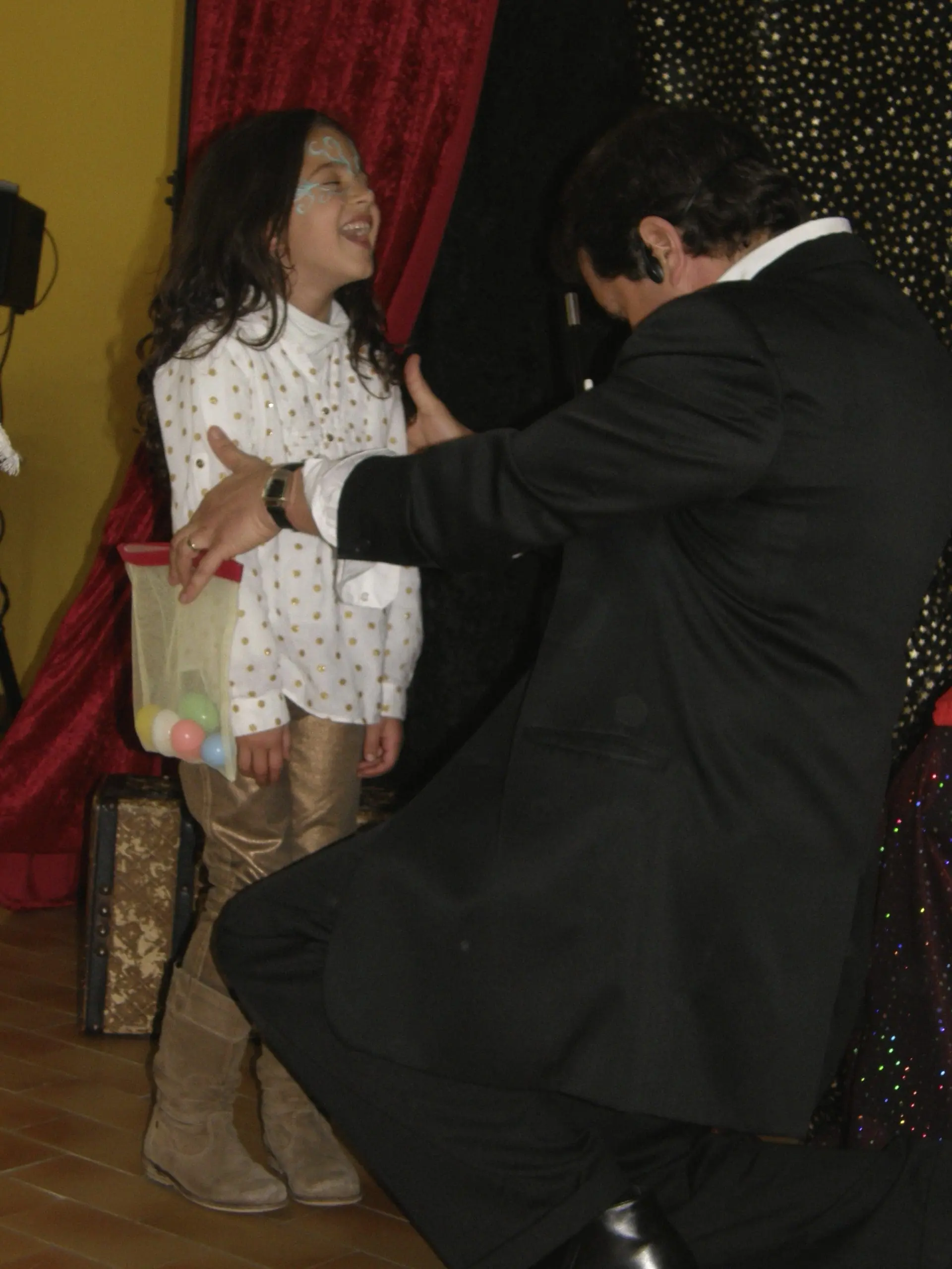 Danny le Magicien en spectacle pour l'anniversaire d'un enfant. Un petite fille rit aux éclats pendant le tour de Magie avec un rideau de théâtre en fond d'image.
